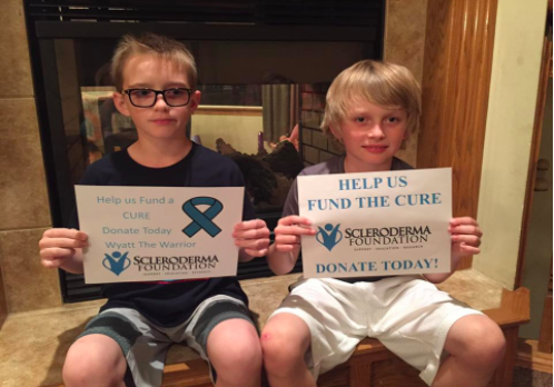 Wyatt (left) and his twin brother, Weston, hold up signs to help find a cure for the Scleroderma foundation.