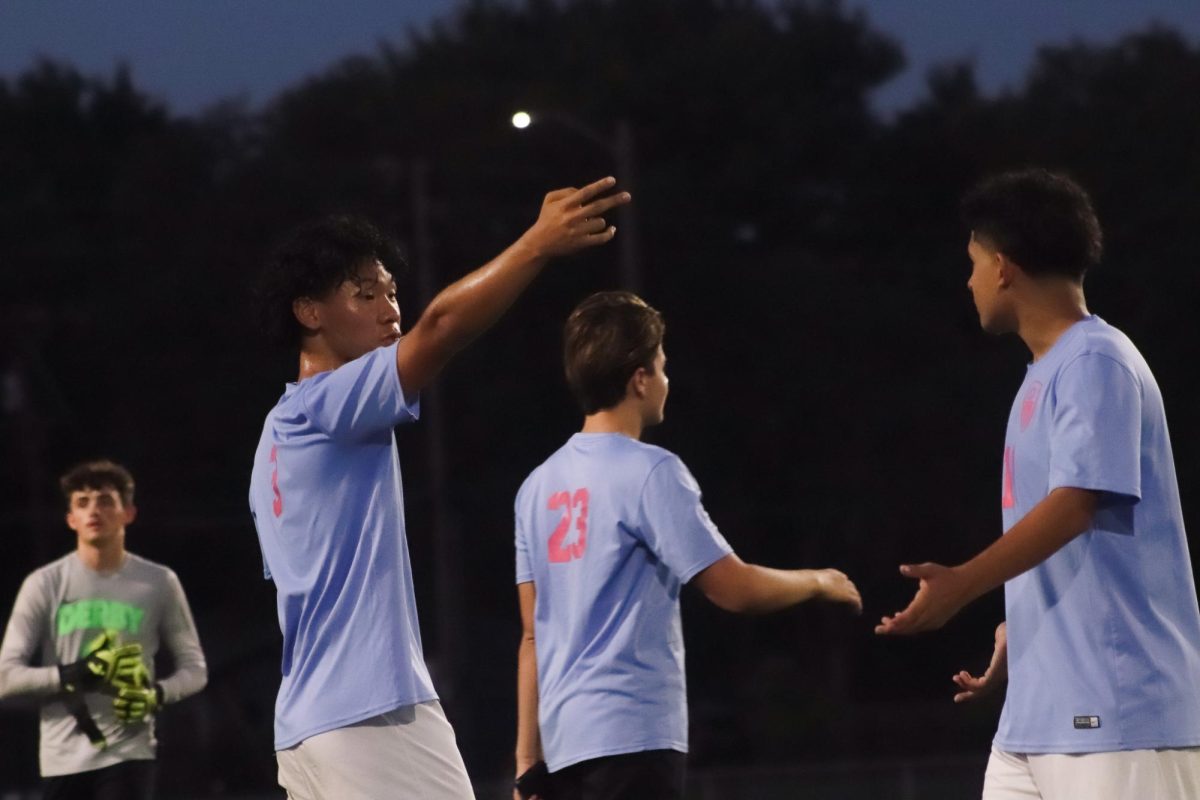 A varsity player hand signals to his teammates while they congratulate eachother.