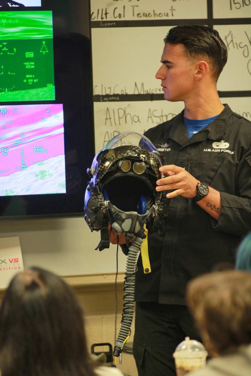 Maintenance crew member holds up the helmet to show to the class what they wear during the plane rides.