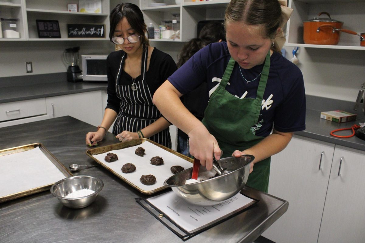 Two students scoop cookies onto a pan.