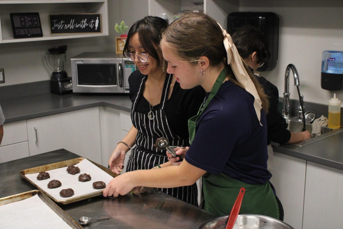 Two students laugh and smile as they look at the cookies they're making.