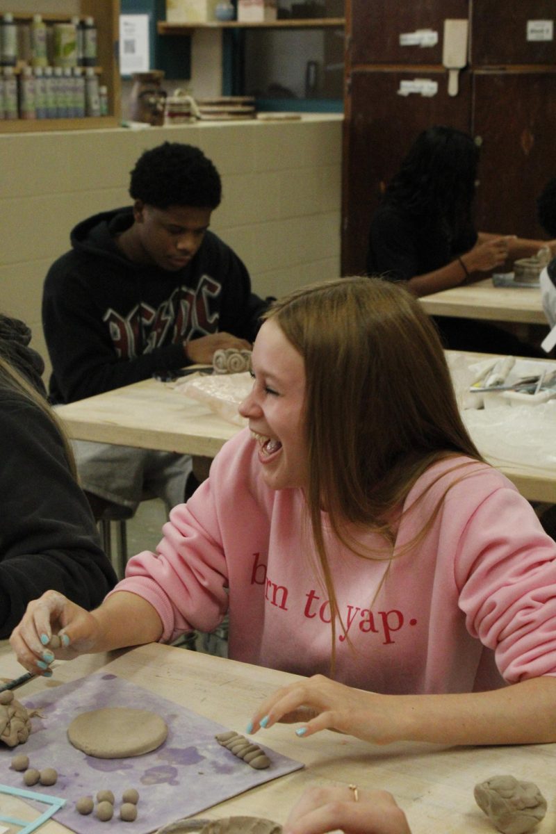 Freshman laughs with friends in clay class.