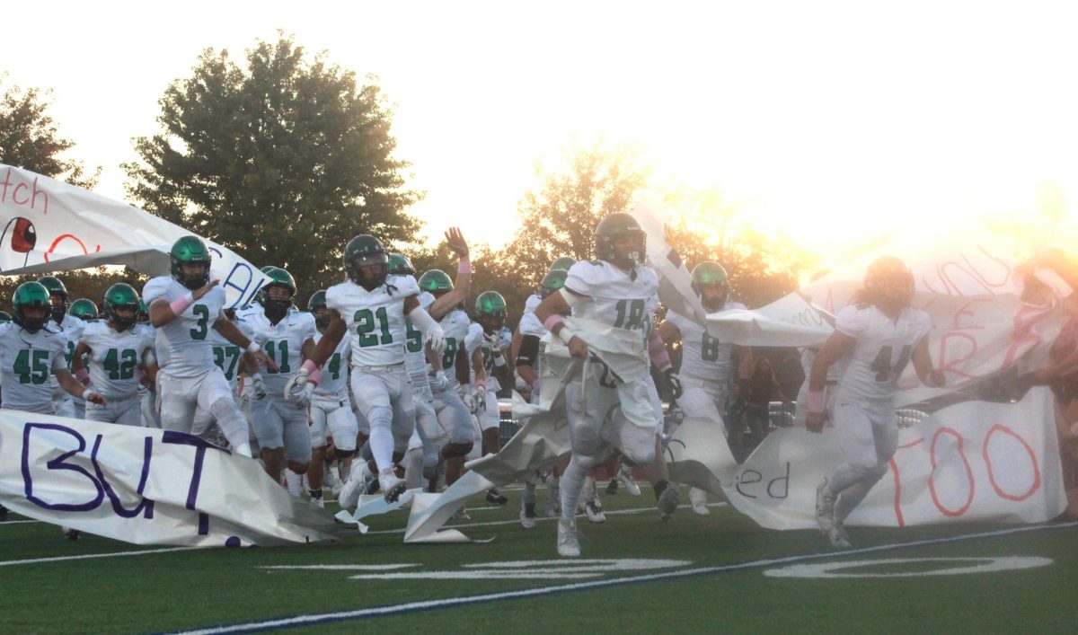 Varsity football runs through the banner that the cheerleaders made.