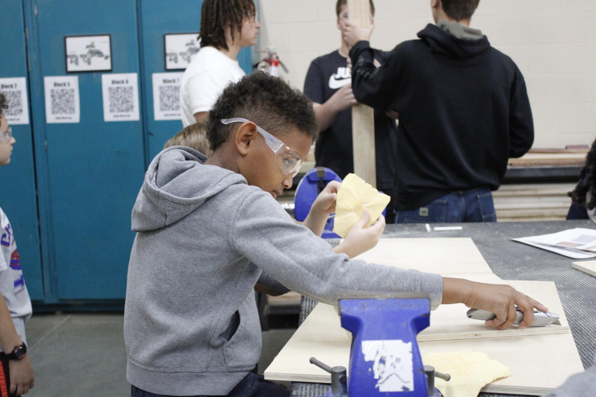 Tanglewood elementary third grader sands down a piece of wood in production methods. 