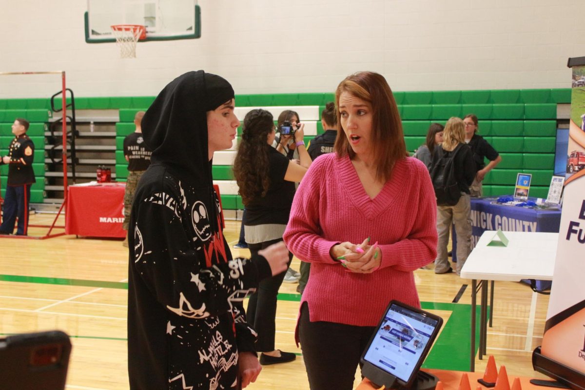 Student talks to college member at college table.