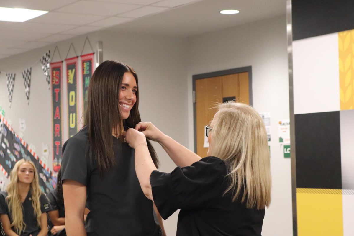 Teacher puts pin on students scrub top. 