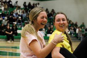 Juniors laugh while riding on scooters across the gym. 