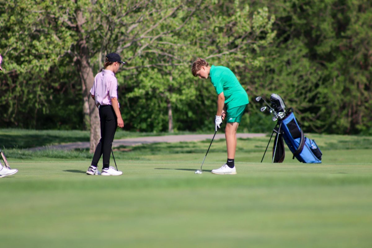 Golfer prepares lines up club with ball. 