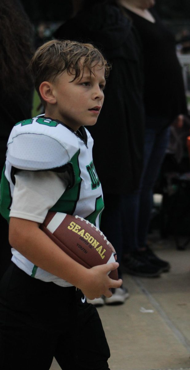 Middle school football player carries a ball through the stands.