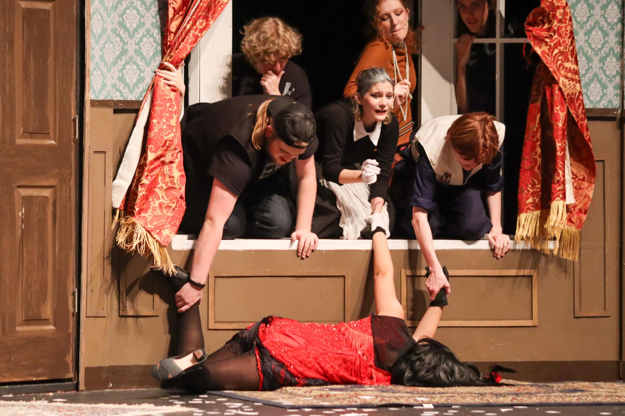 Performers collaborate to try and get actress who is unconscious off stage through the window.