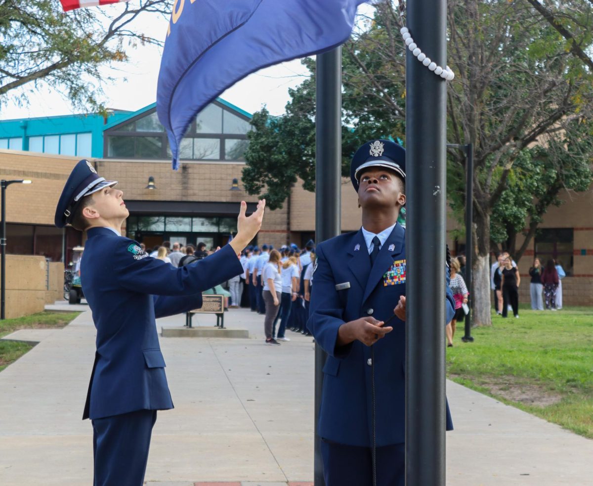 AFJROTC member holds hands up to flag while other member lowers it.