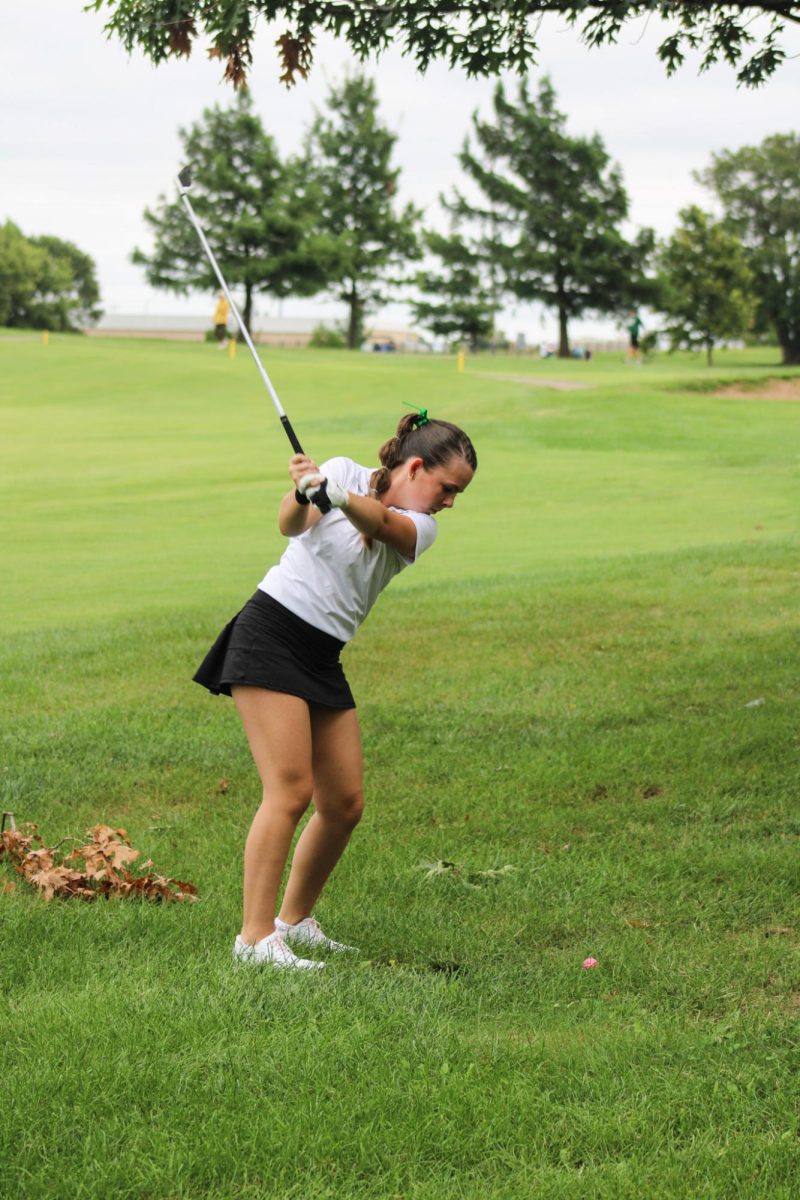 Golfer swings club to hit the ball. 