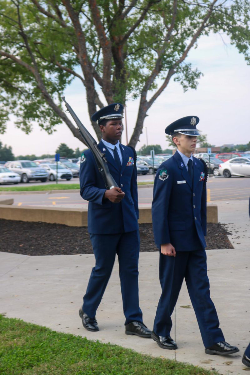 ROTC members walk while one holds the rifle. 