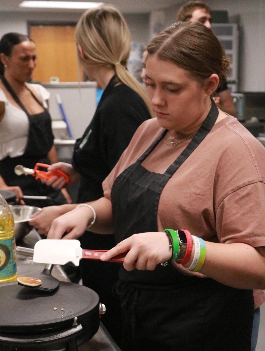 Student flips her mini pancakes with two spatulas.