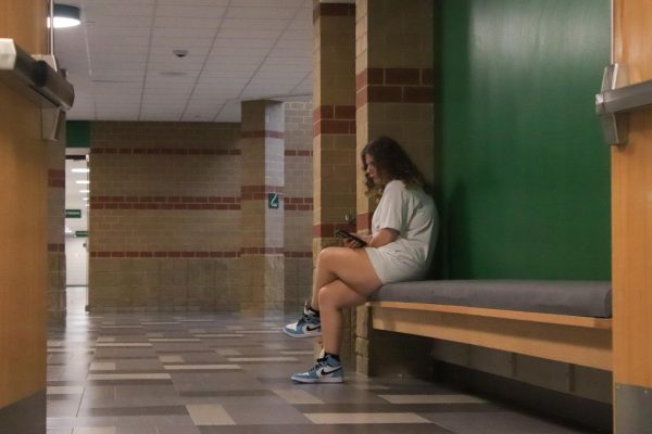 Student sits in bench in hallway.