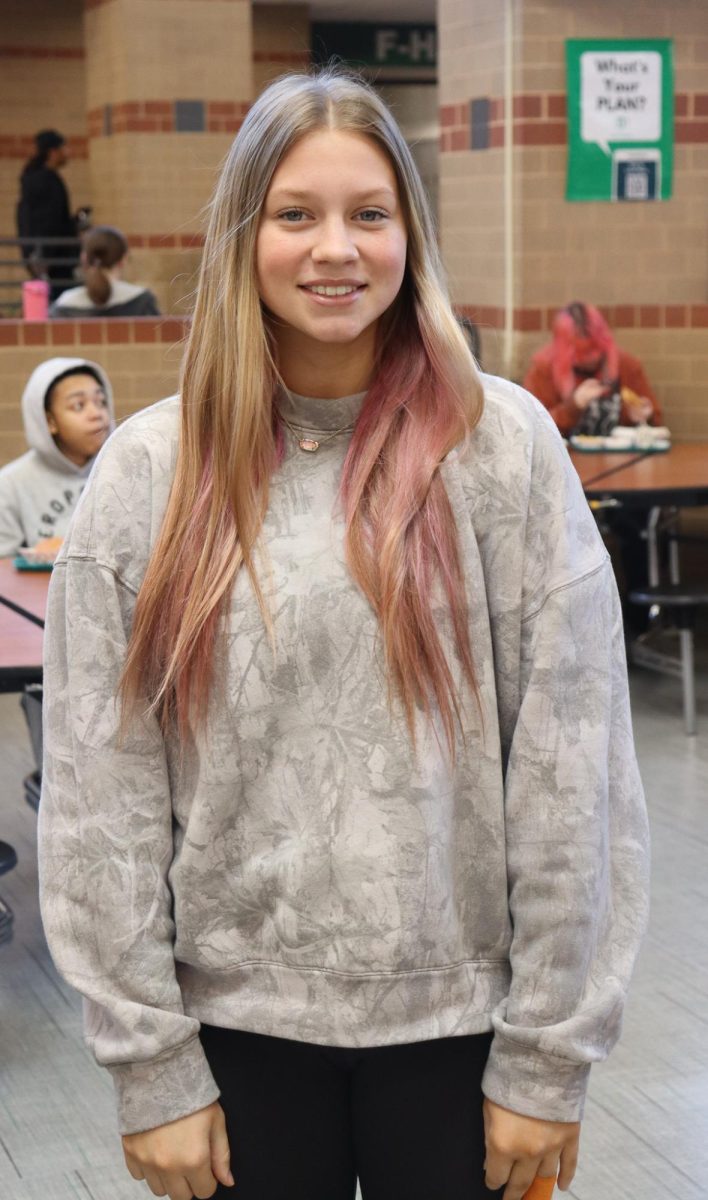 Student poses for a photo while wearing a camo crewneck.